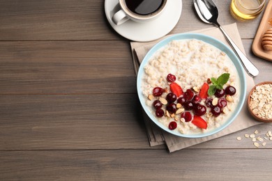 Bowl of oatmeal porridge served with berries on wooden table, flat lay. Space for text