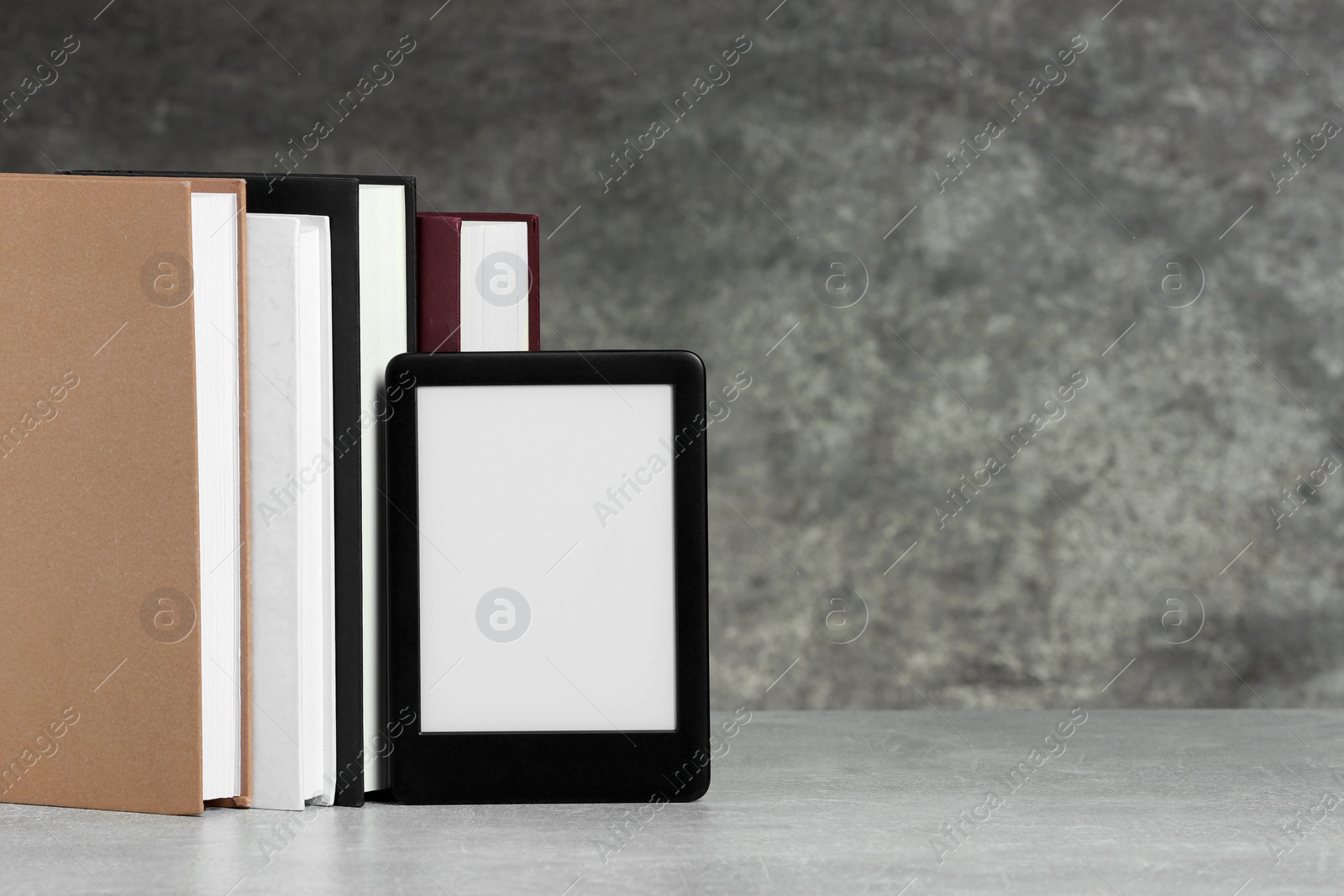 Photo of Portable e-book reader and many hardcover books on white textured table, space for text