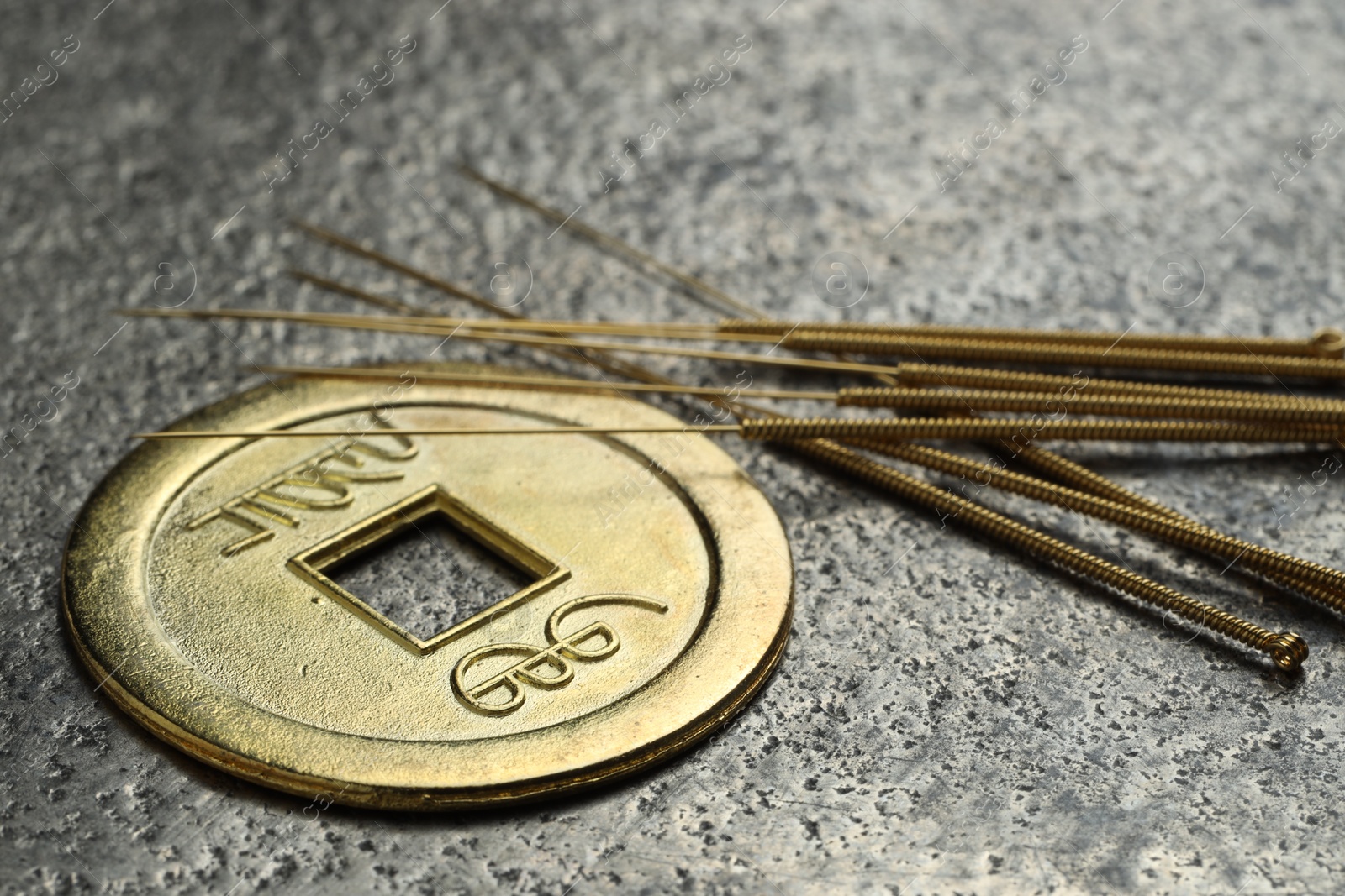 Photo of Acupuncture needles and Chinese coin on grey textured table, closeup