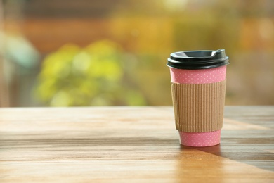 Cardboard cup of coffee on table against blurred background. Space for text