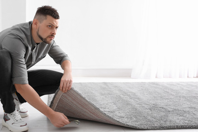 Worried man hiding money under carpet indoors. Financial savings