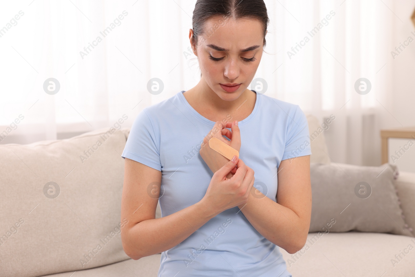 Photo of Woman putting sticking plaster onto hand at home