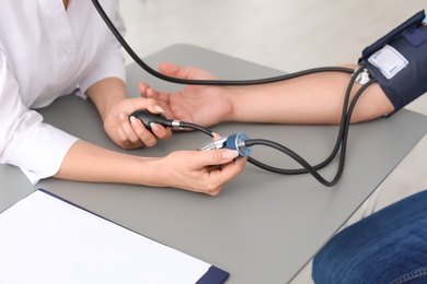 Doctor checking patient's blood pressure at table in office