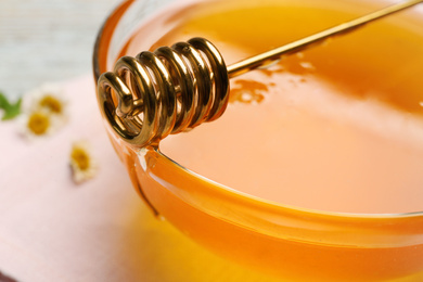 Photo of Tasty honey in glass bowl and dipper on table, closeup
