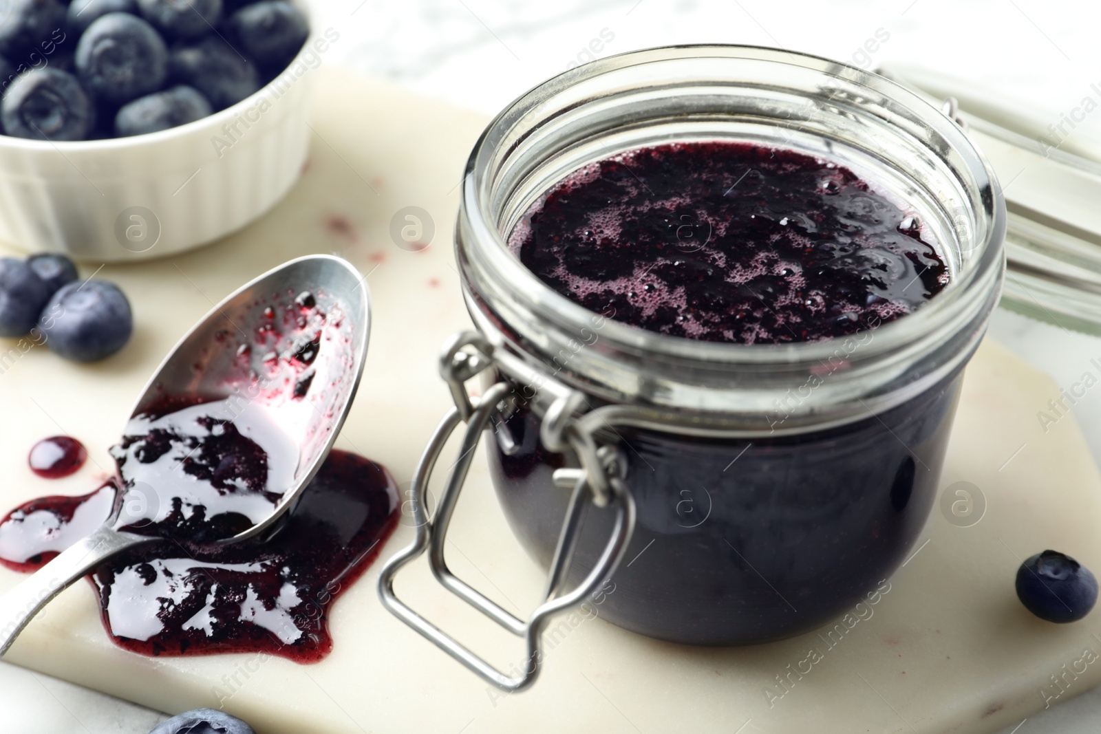 Photo of Jar of blueberry jam and fresh berries on table, closeup