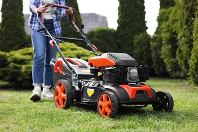Photo of Woman cutting green grass with lawn mower in garden, selective focus
