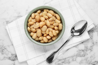 Bowl of canned kidney beans and spoon on white marble table, top view