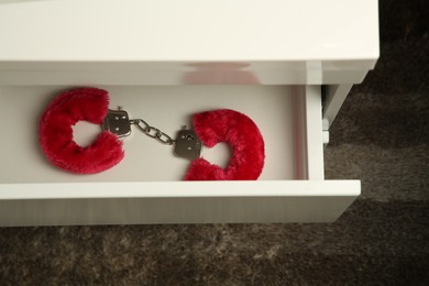 Photo of Red furry handcuffs in drawer indoors, above view. Sex toy