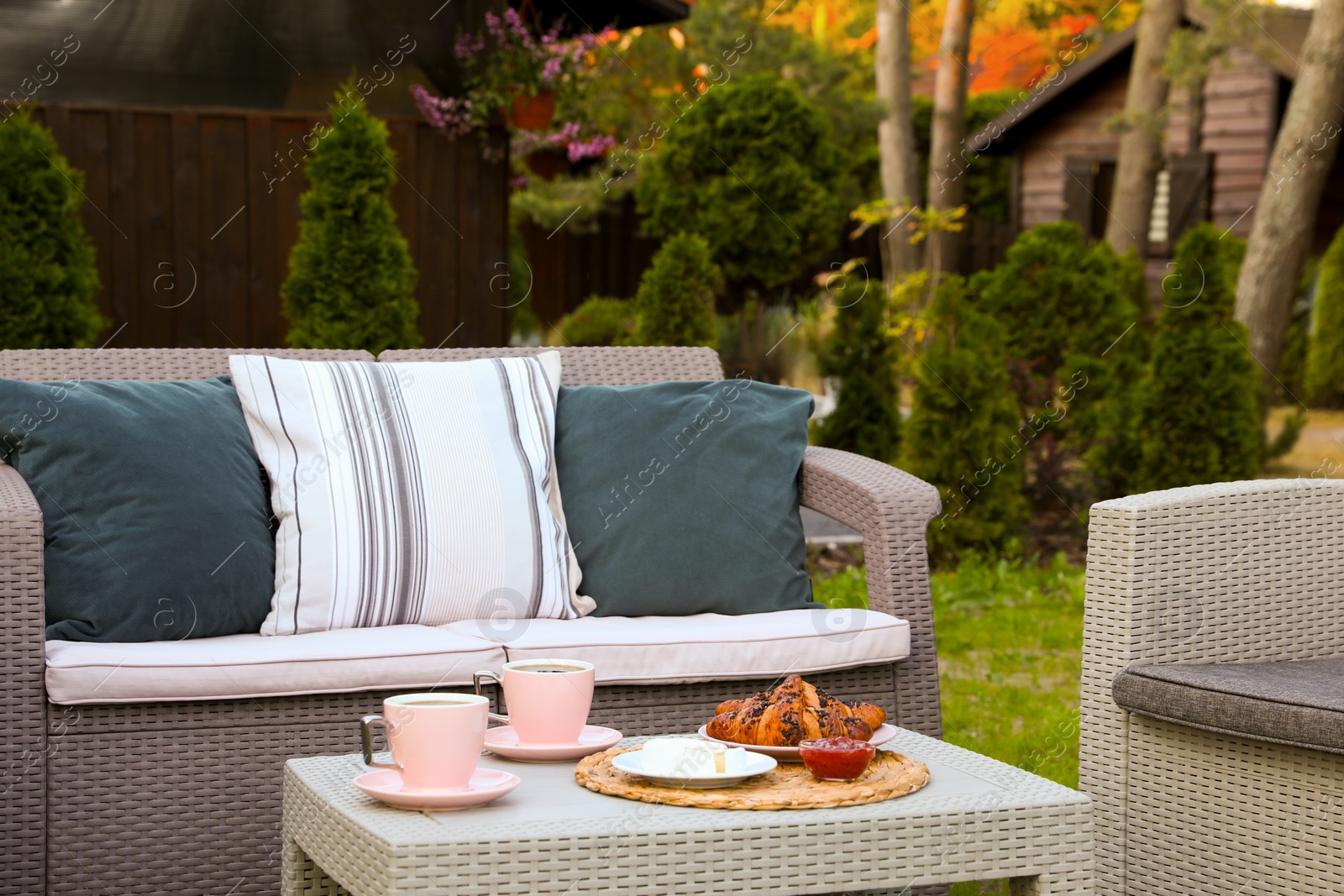 Outdoor breakfast with tea and croissants on rattan table in garden Photo of Outdoor breakfast with tea and croissants on rattan table in garden