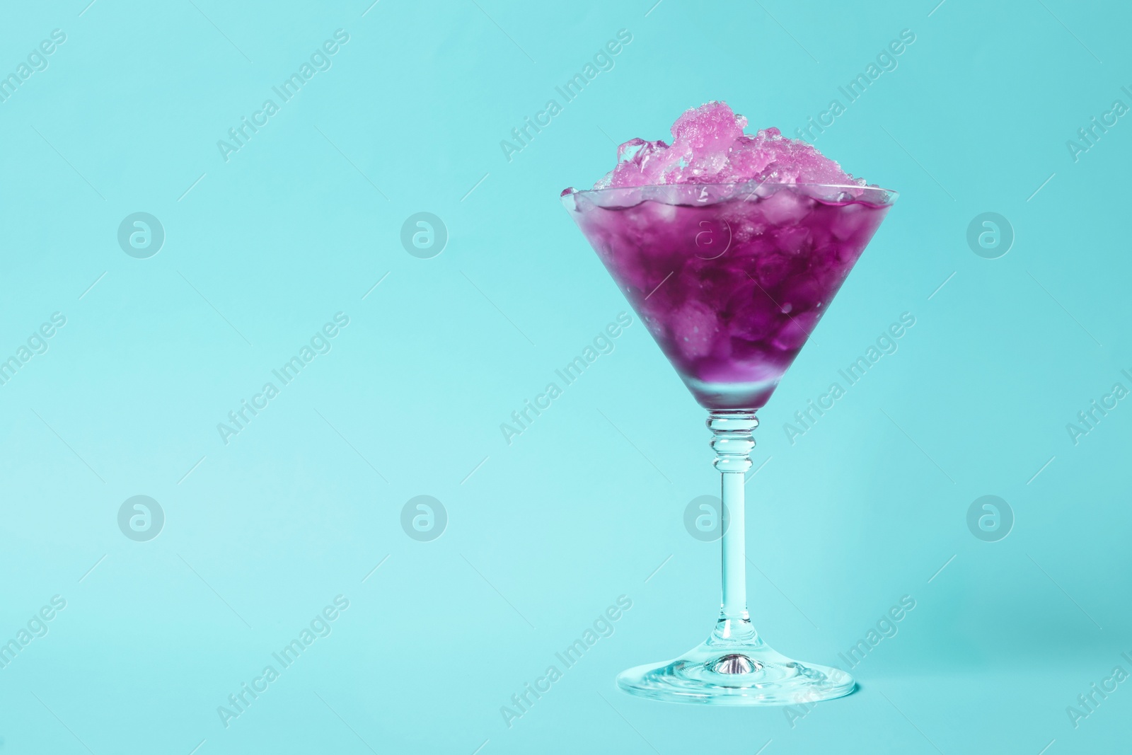 Photo of Shaving ice in martini glass on light blue background, space for text