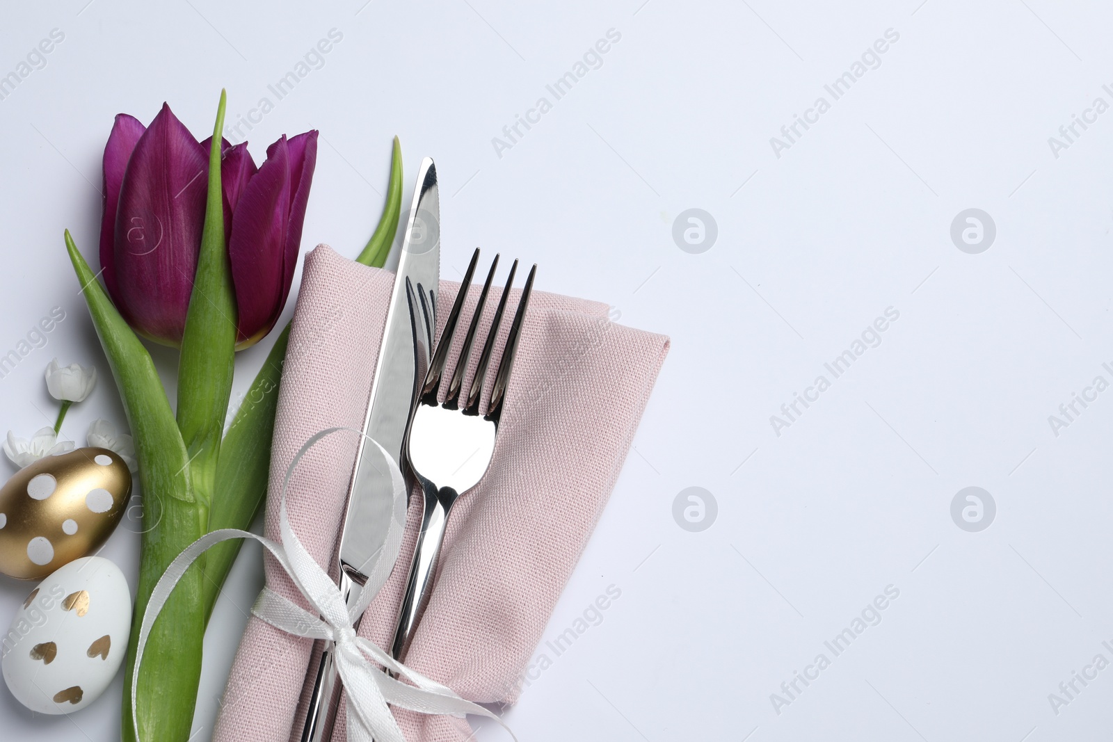 Photo of Cutlery set, Easter eggs and tulip on white background, flat lay with space for text. Festive table setting