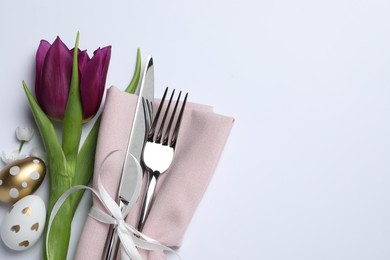 Photo of Cutlery set, Easter eggs and tulip on white background, flat lay with space for text. Festive table setting