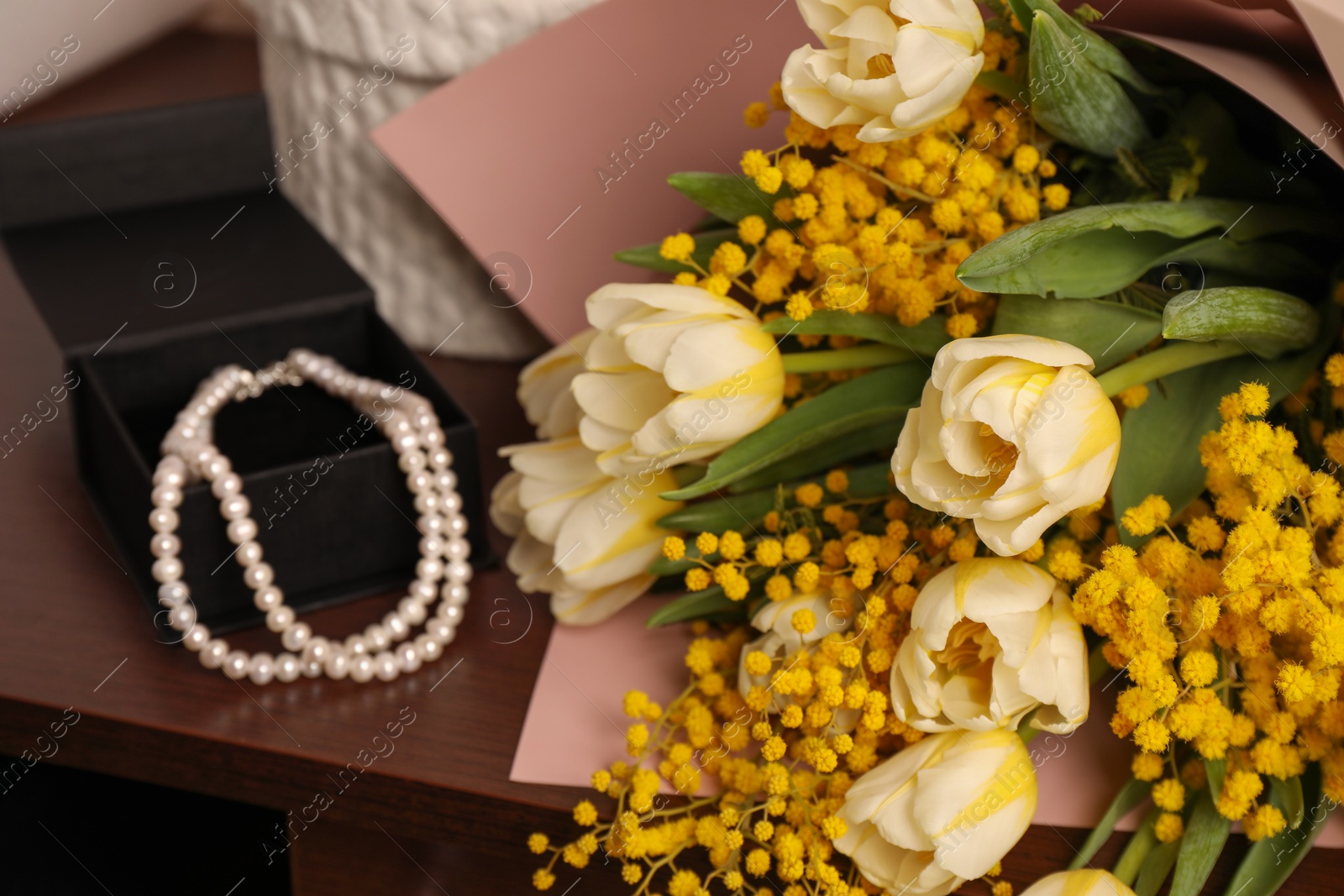 Photo of Bouquet with beautiful spring flowers and necklace on wooden chest of drawers, closeup