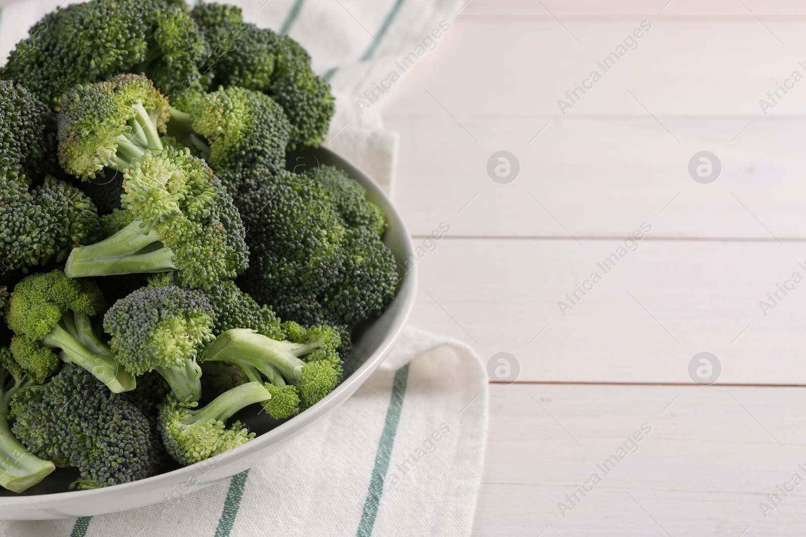 Photo of Bowl of fresh raw broccoli on white wooden table, closeup. Space for text