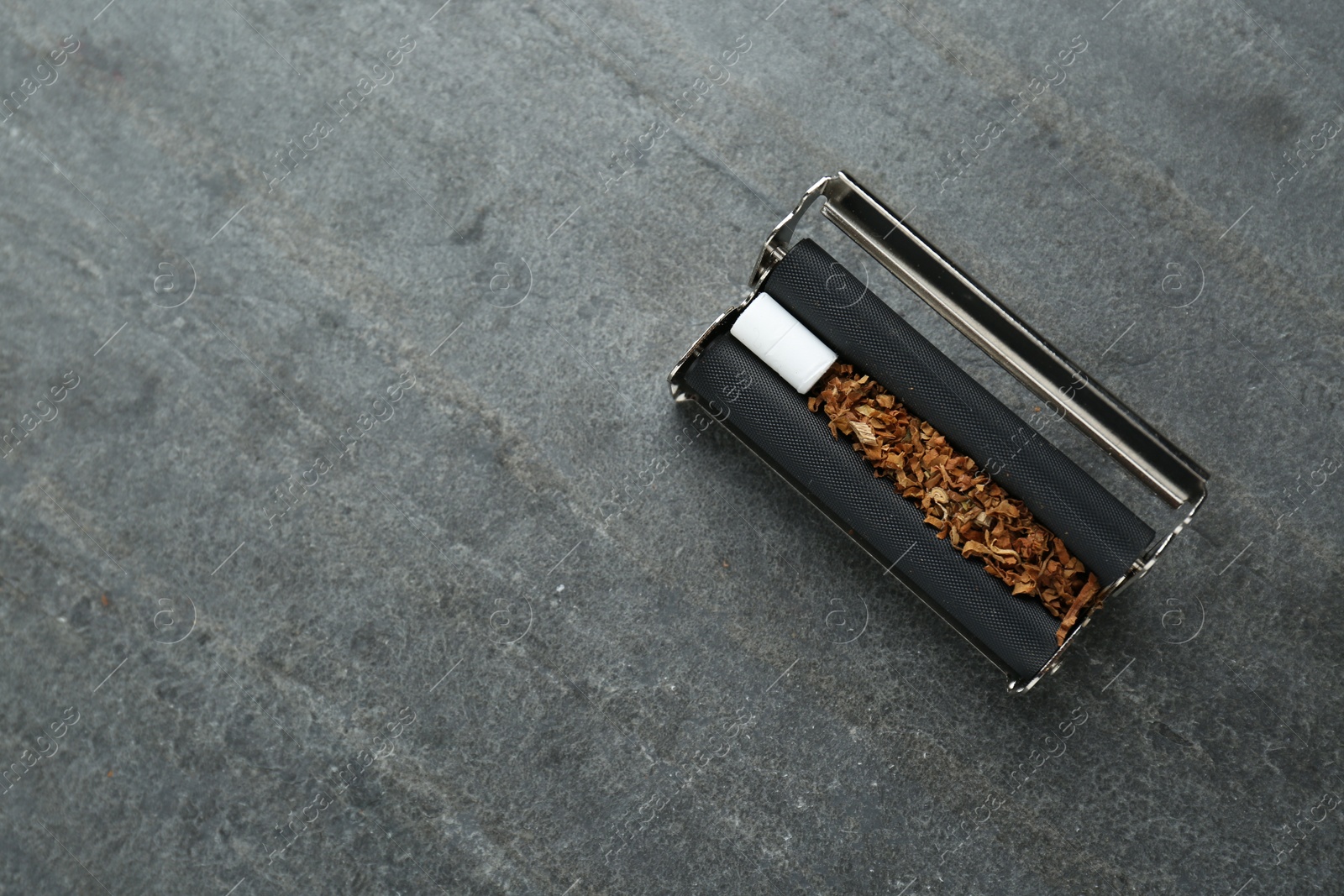 Photo of Cigarette roller with tobacco and filter on grey table, top view. Space for text