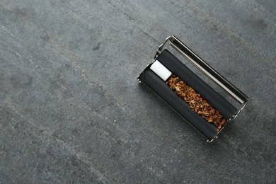 Photo of Cigarette roller with tobacco and filter on grey table, top view. Space for text