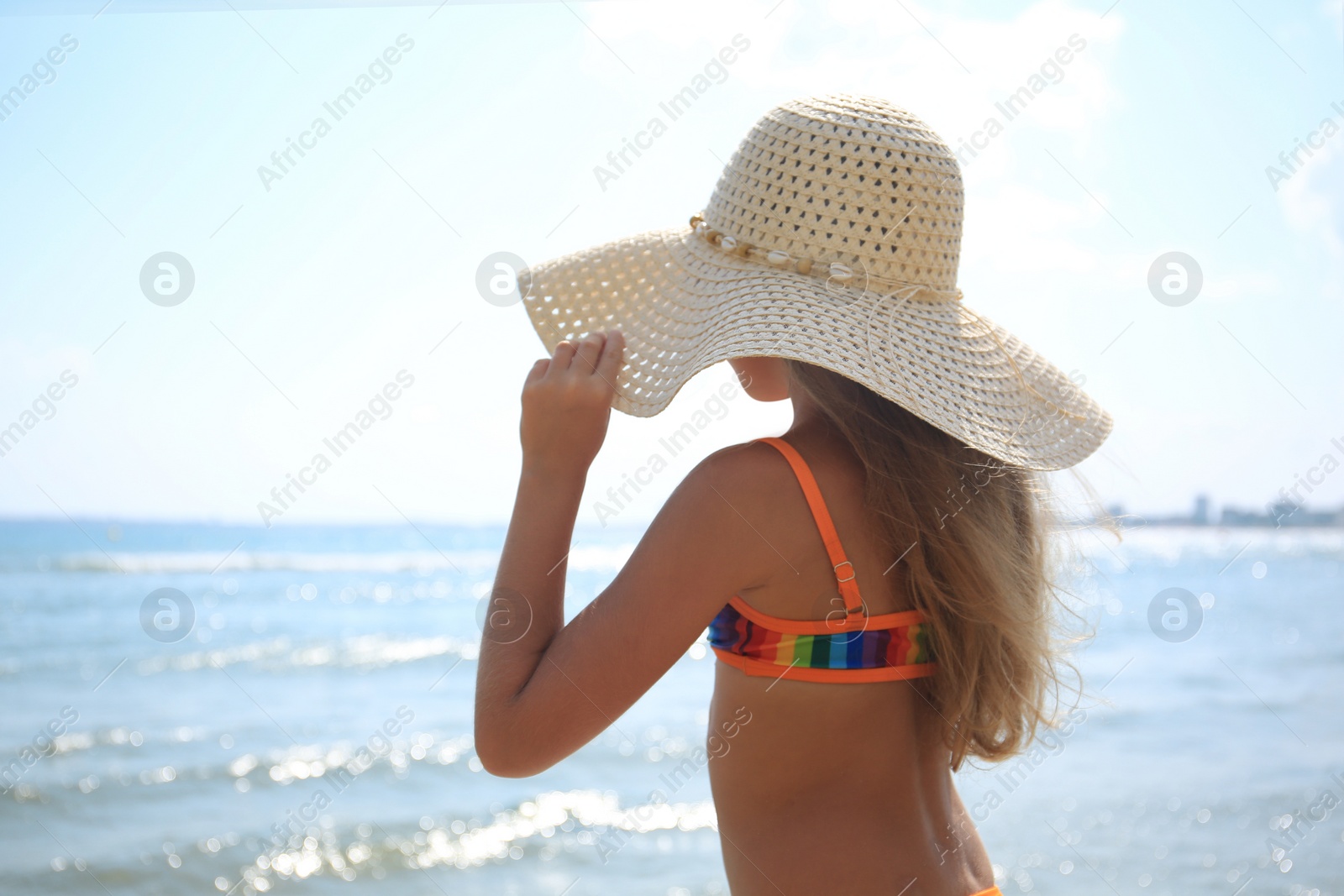 Photo of Little girl in stylish hat on beach near sea