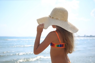 Photo of Little girl in stylish hat on beach near sea