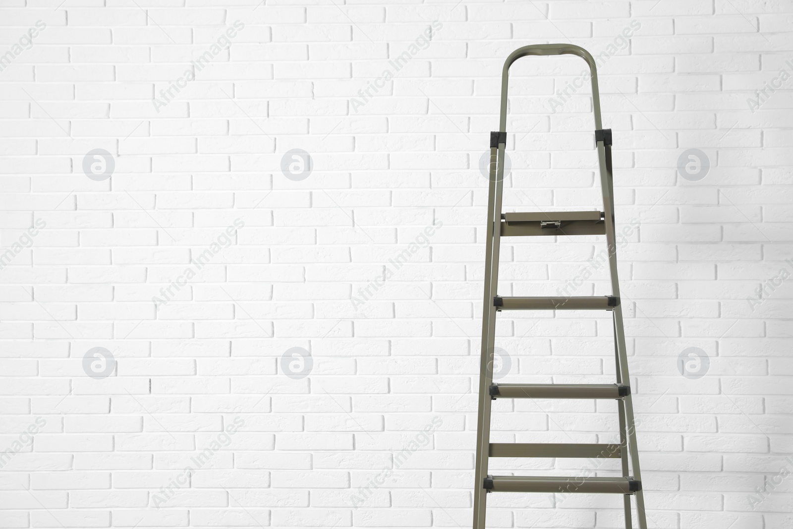 Photo of Metal stepladder near white brick wall. Space for text