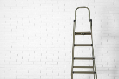 Metal stepladder near white brick wall. Space for text