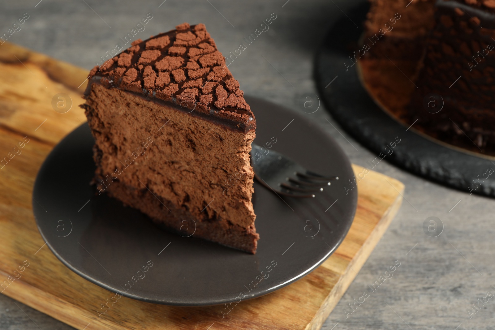 Photo of Piece of delicious chocolate truffle cake and fork on grey textured table, closeup