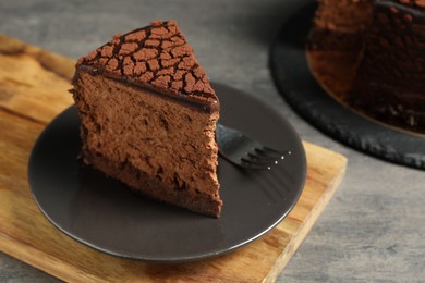 Piece of delicious chocolate truffle cake and fork on grey textured table, closeup