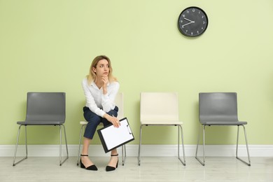 Photo of Young woman with clipboard waiting for job interview indoors