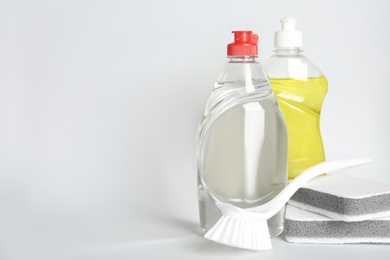 Photo of Detergents, brush and sponges on light background, space for text. Clean dishes