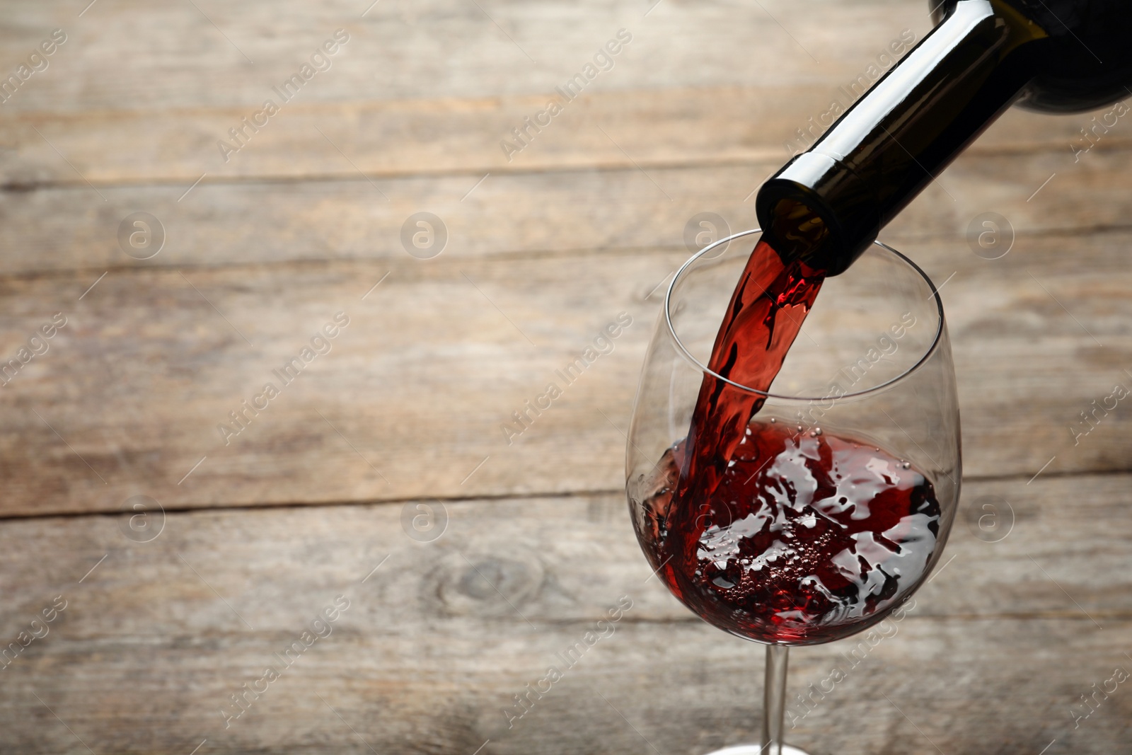 Photo of Pouring red wine from bottle into glass on wooden background. Space for text