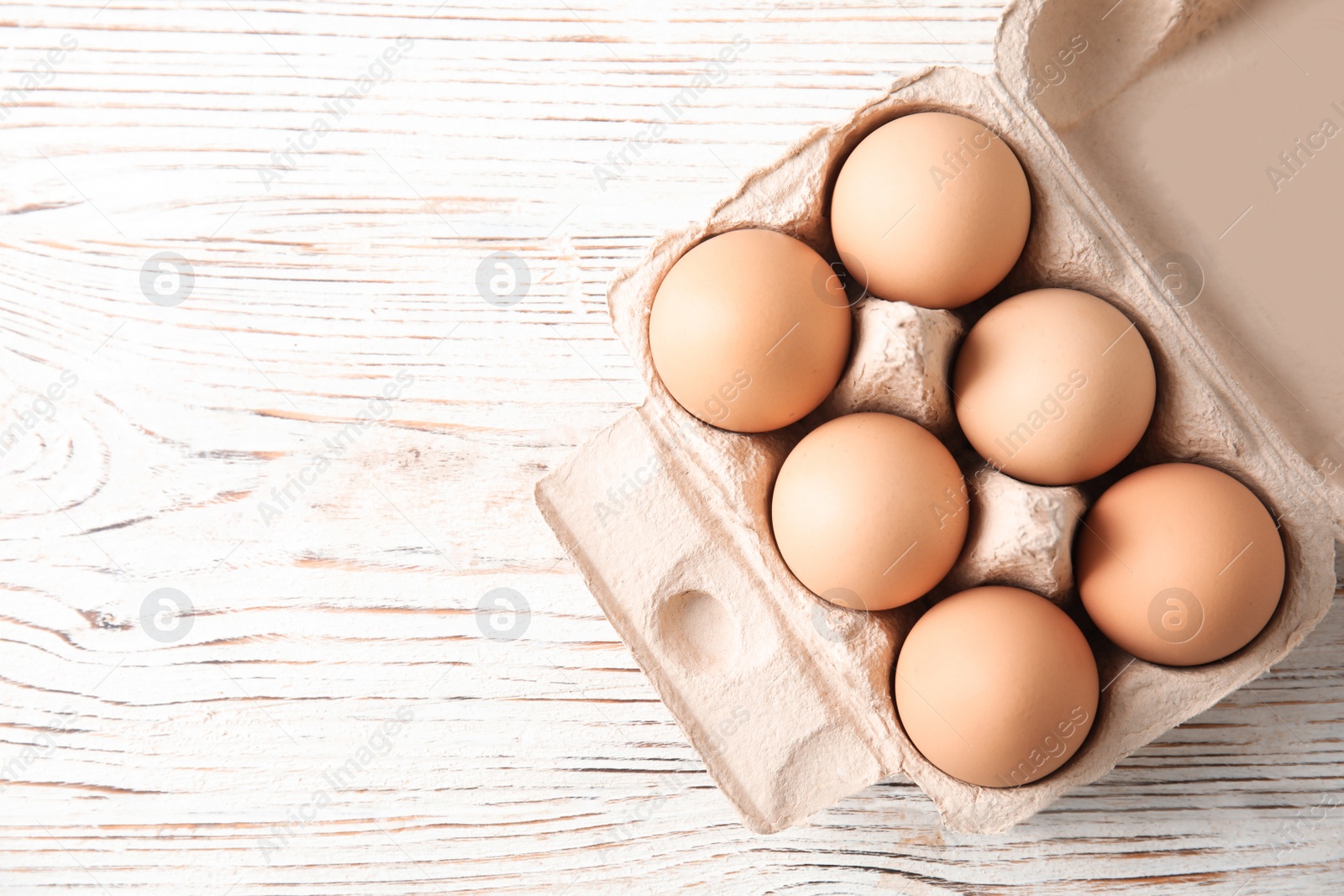 Photo of Carton of raw chicken eggs on wooden background, top view. Space for text