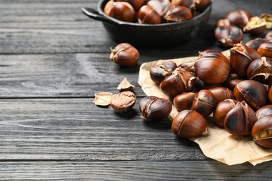 Photo of Tasty roasted edible chestnuts on black wooden table, closeup. Space for text
