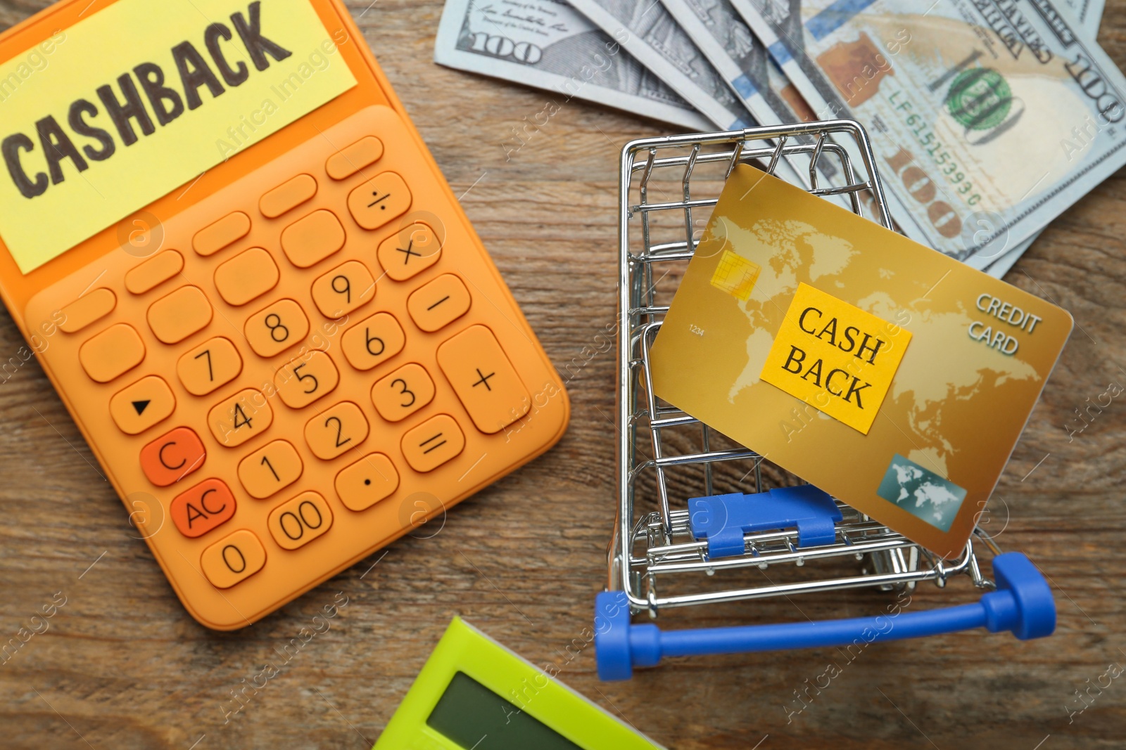 Photo of Calculators, dollar banknotes and credit card in shopping cart on wooden background, flat lay with space for text. Cashback concept