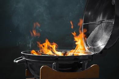 Photo of New modern barbecue grill with burning firewood on dark background