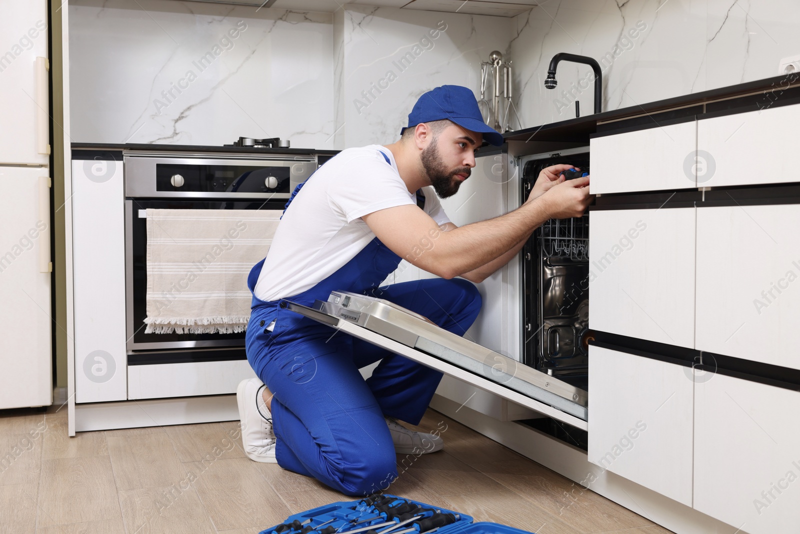 Photo of Serviceman repairing dishwasher with screwdriver in kitchen