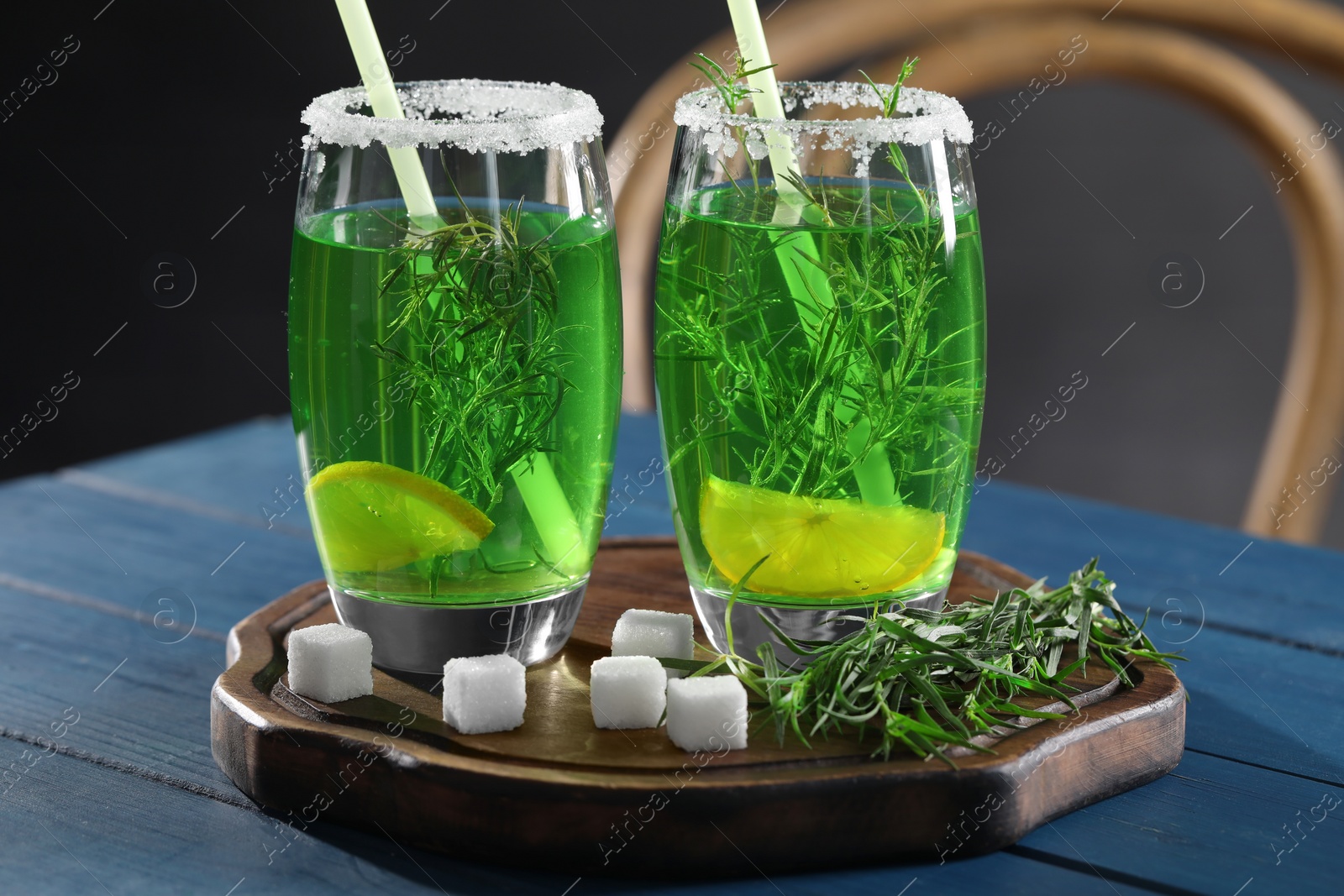 Photo of Glasses of homemade refreshing tarragon drink, sprigs and sugar cubes on blue wooden table, closeup