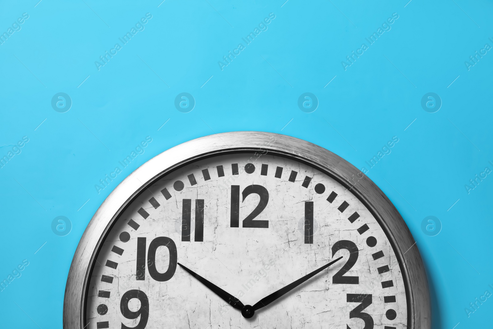 Photo of Stylish analog clock hanging on light blue wall, space for text