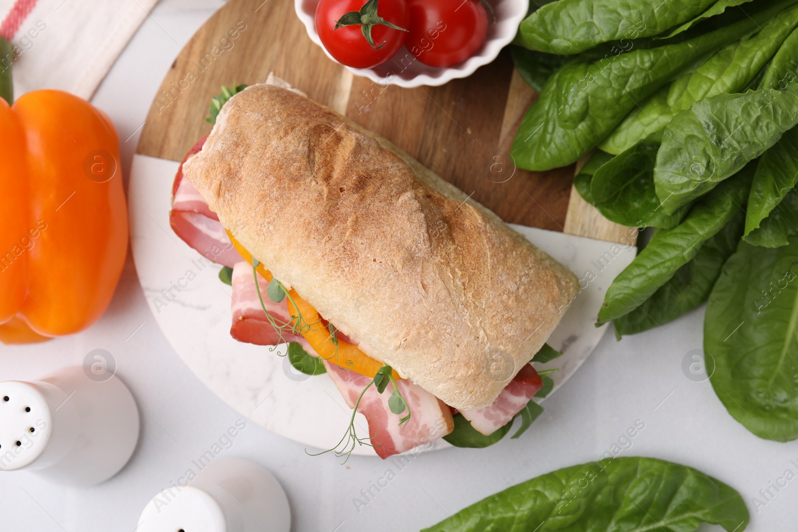 Photo of Tasty sandwich with bacon, tomatoes, greens and bell pepper on white tiled table, flat lay