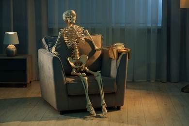 Waiting concept. Human skeleton sitting in armchair indoors