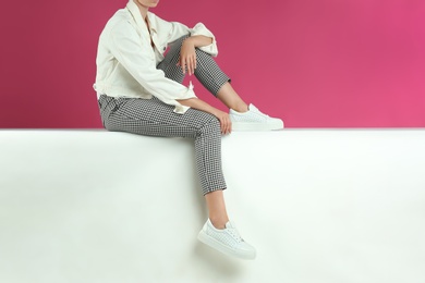 Woman in stylish shoes sitting on color background, closeup