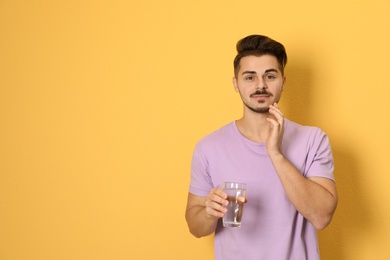 Photo of Young man with sensitive teeth and glass of water on color background. Space for text