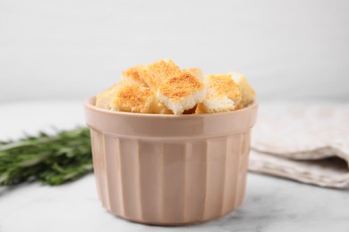Photo of Delicious crispy croutons in bowl on white marble table, closeup