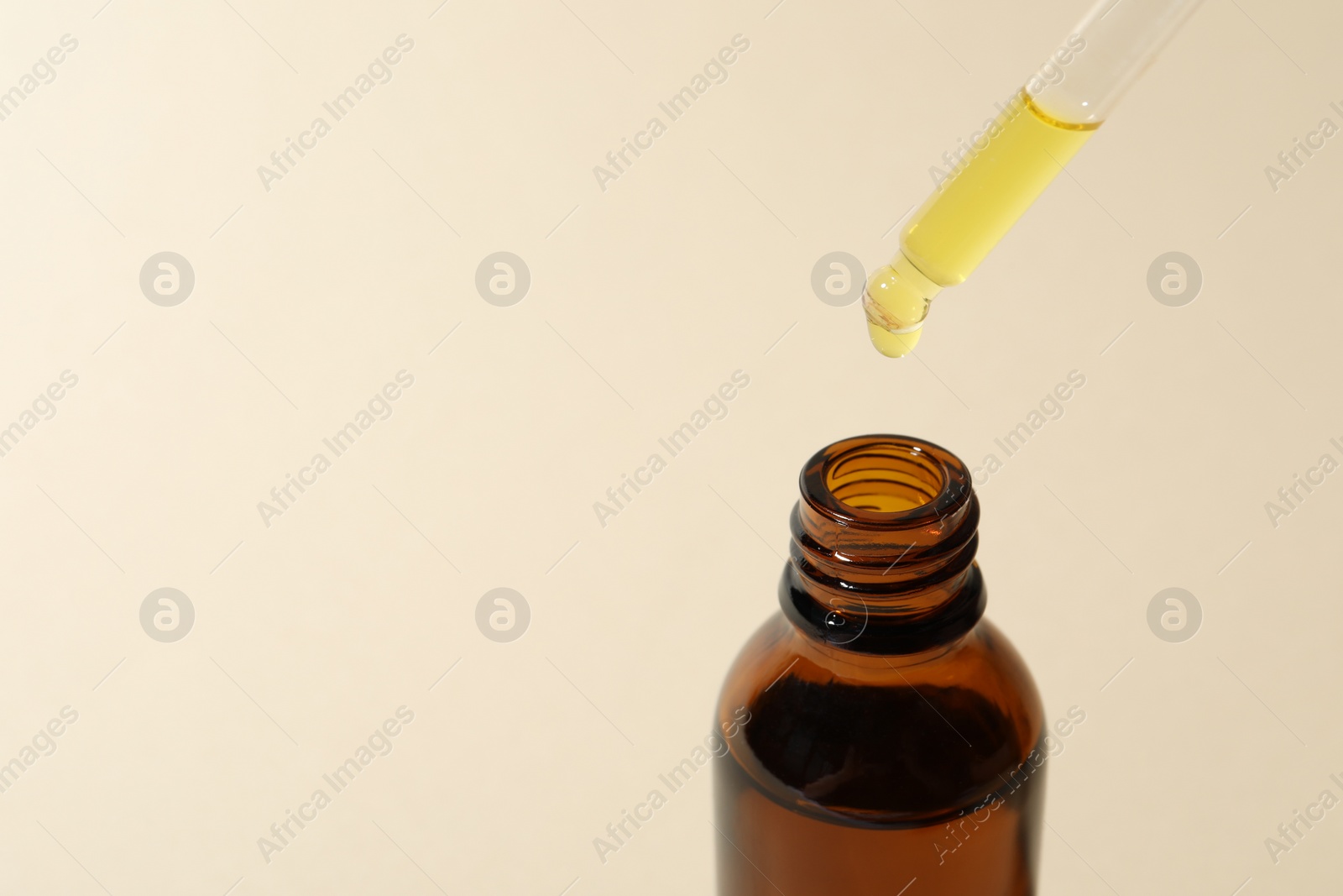 Photo of Dripping cosmetic oil from pipette into bottle on beige background, closeup. Space for text