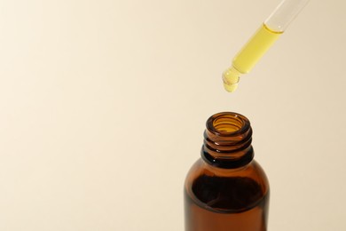 Photo of Dripping cosmetic oil from pipette into bottle on beige background, closeup. Space for text