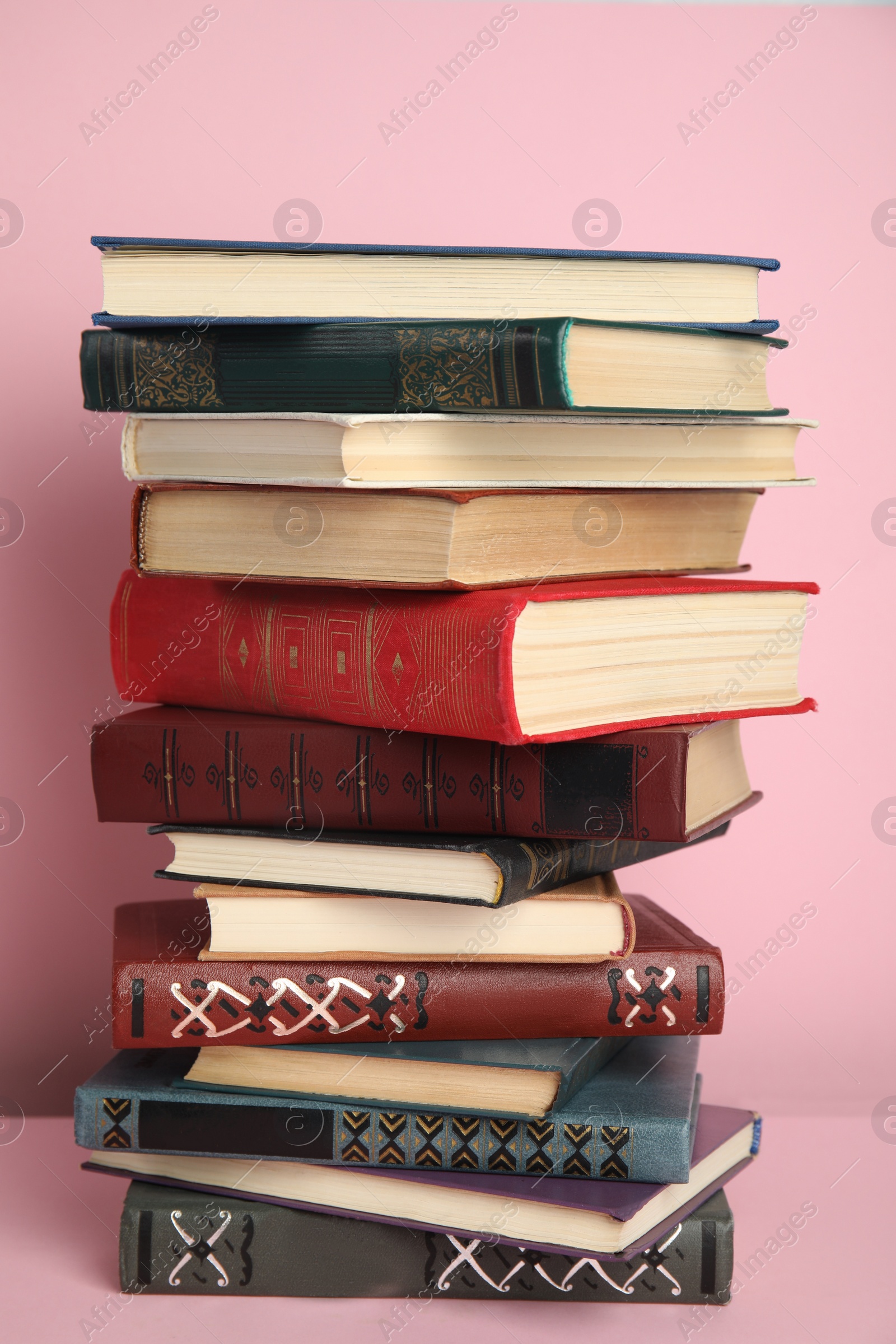 Photo of Stack of different hardcover books on pink background