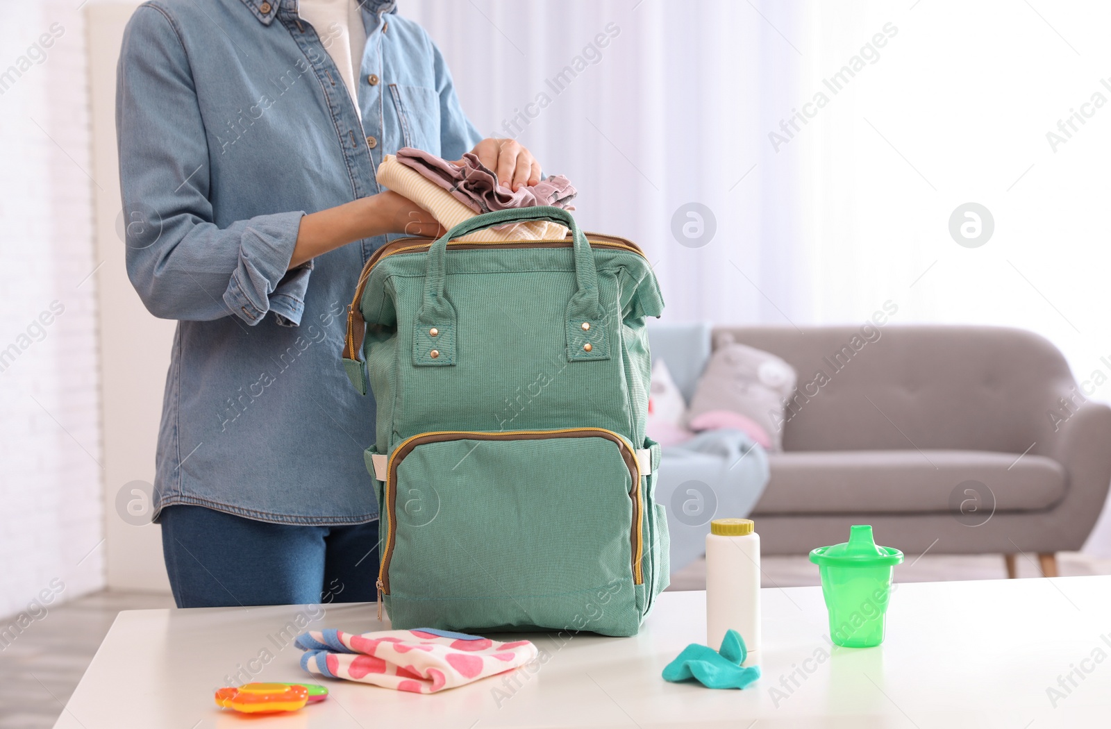 Photo of Woman packing baby accessories into maternity backpack on table indoors, closeup