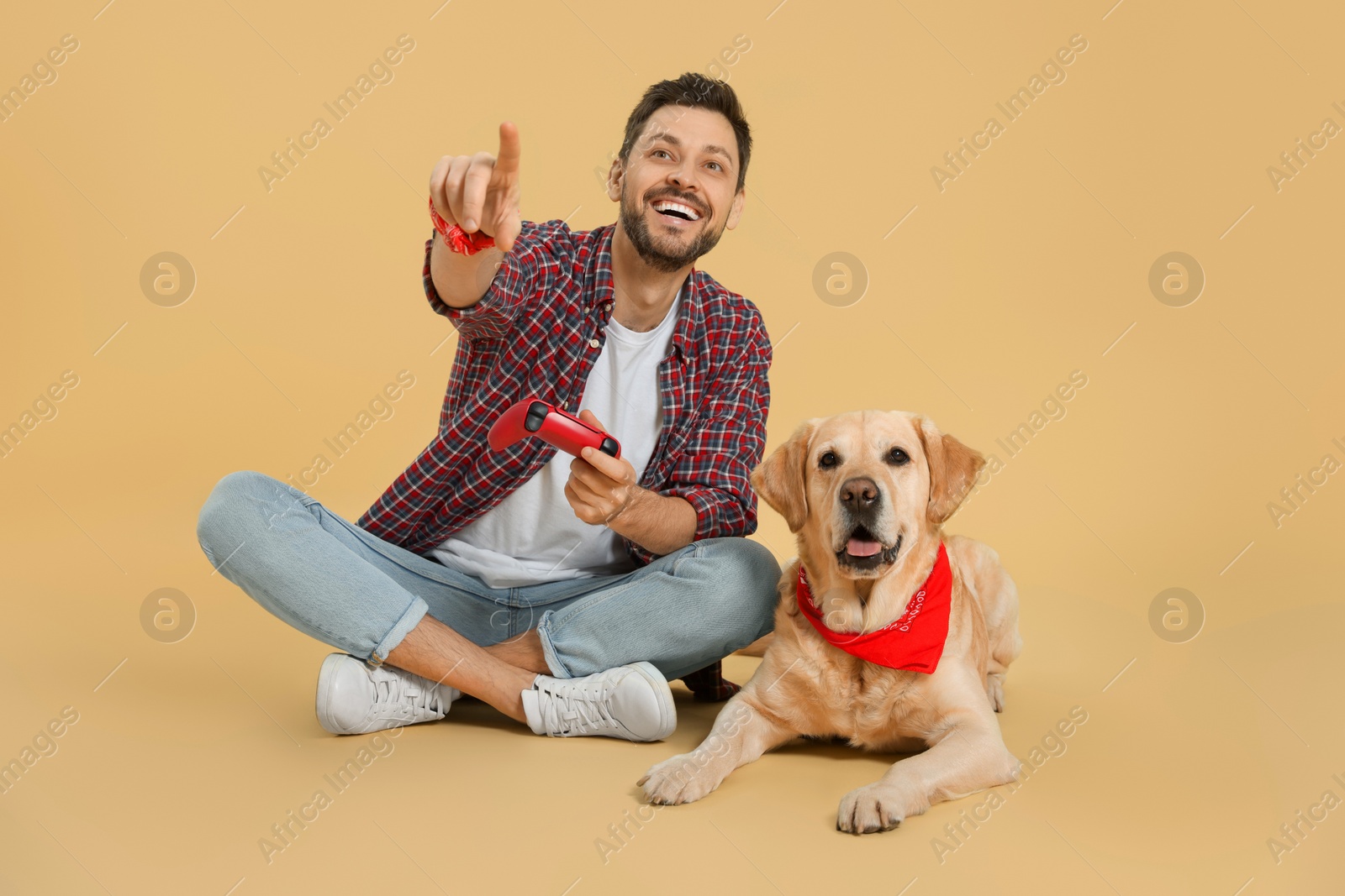 Photo of Happy man playing game with controller near his cute Labrador Retriever on beige background