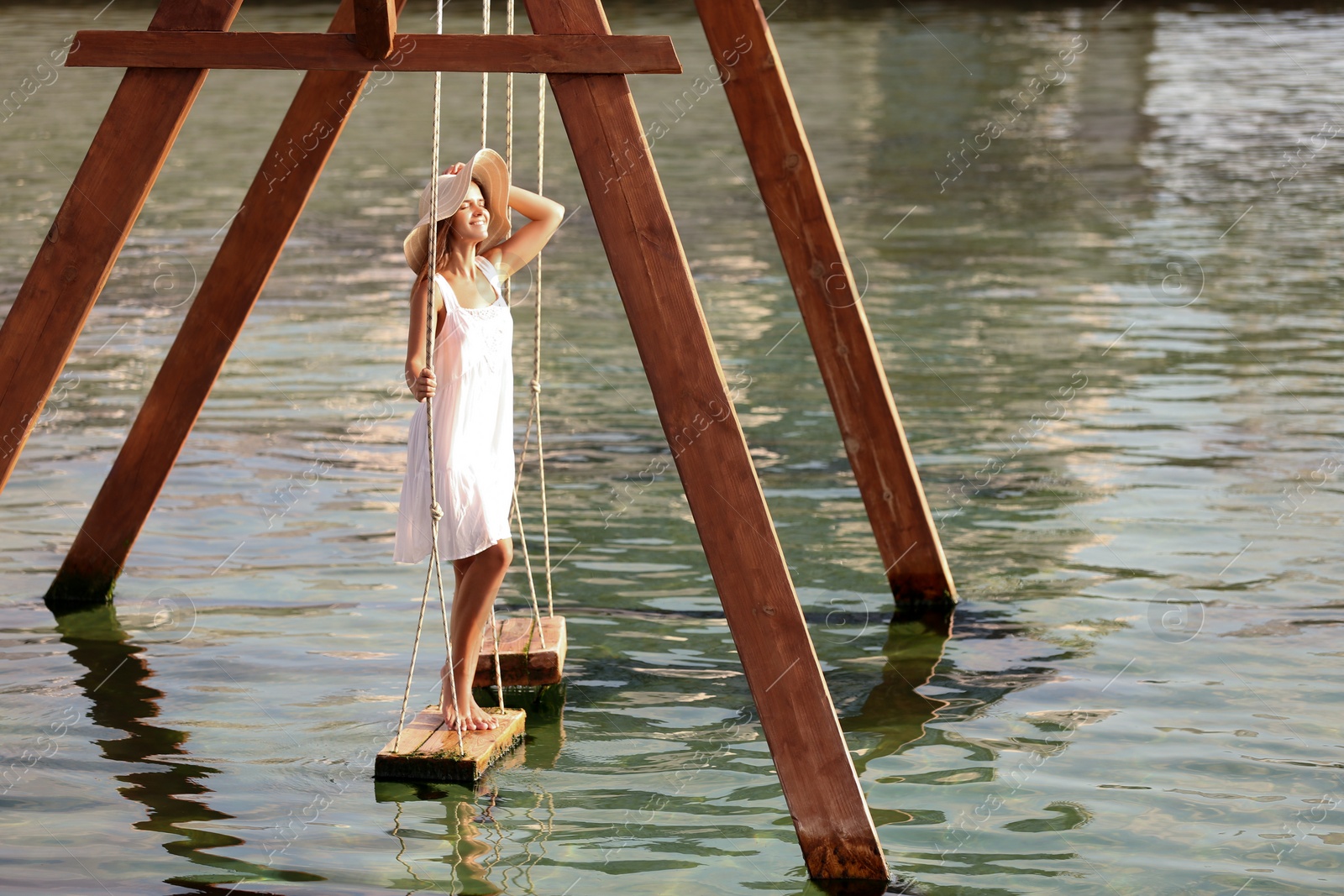 Photo of Young woman on swing over water on sunny day