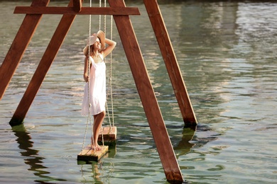 Young woman on swing over water on sunny day