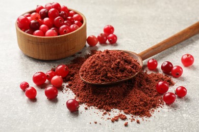 Photo of Pile of cranberry powder, spoon and fresh berries on light grey table