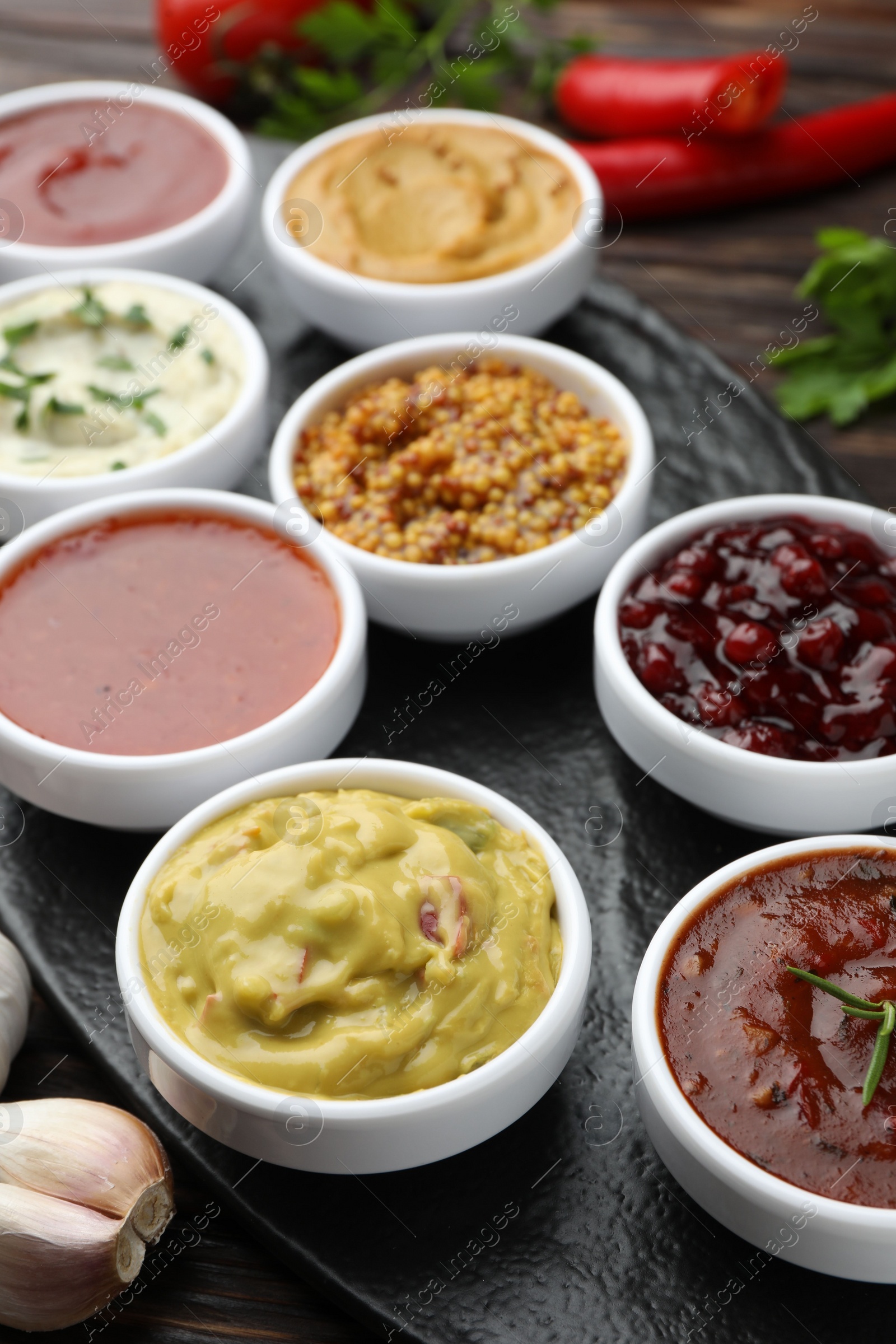 Photo of Different tasty sauces in bowls and garlic on table, closeup